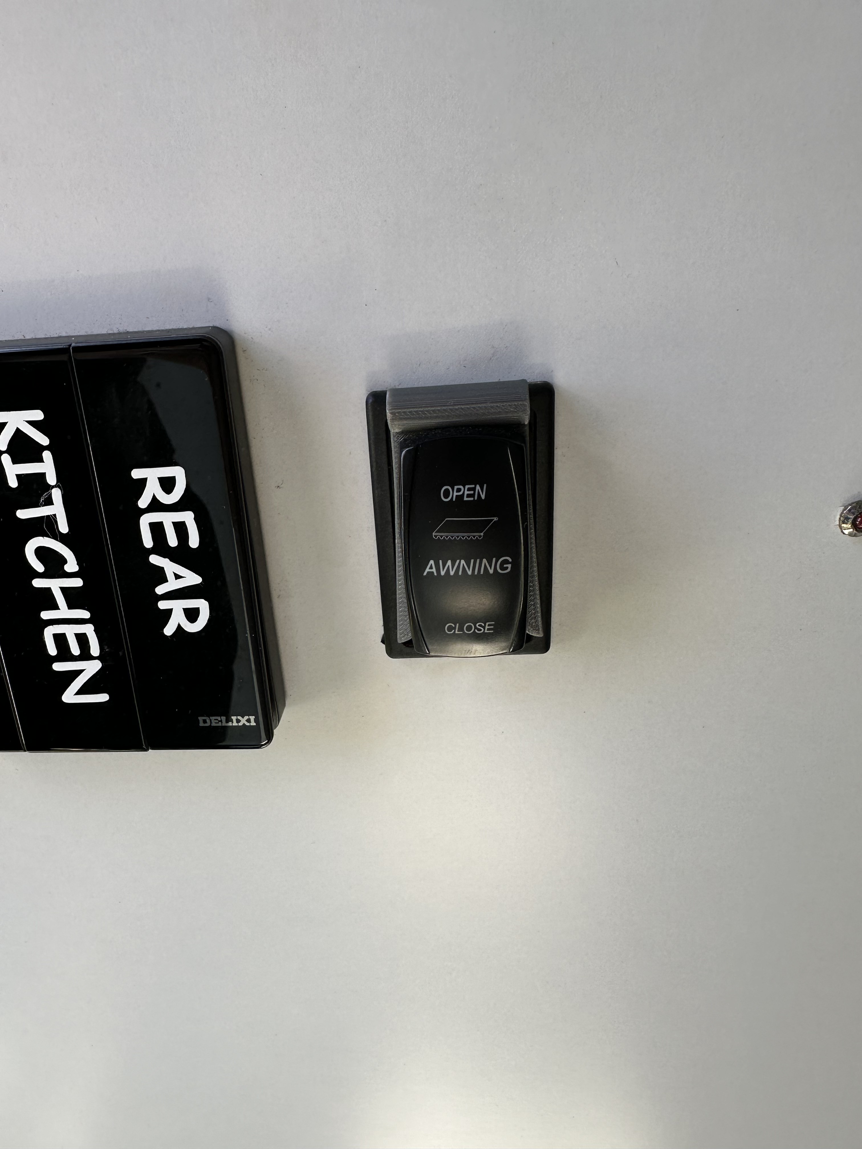 Grey 3D-printed awning switch stopper fitted around a black Scout 15 rocker switch